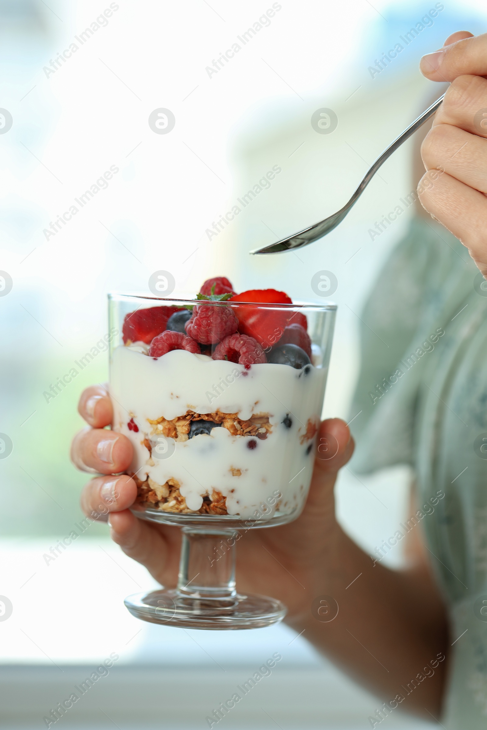 Photo of Woman eating tasty yogurt with fresh berries and granola indoors, closeup