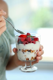 Photo of Woman eating tasty yogurt with fresh berries and granola indoors, closeup