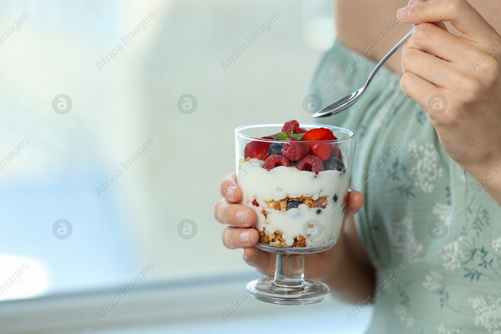 Photo of Woman eating tasty yogurt with fresh berries and granola indoors, closeup. Space for text