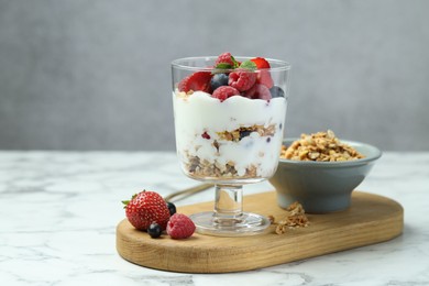 Tasty yogurt with fresh berries and granola in glass dessert bowl on white marble table, space for text