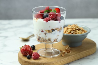 Photo of Tasty yogurt with fresh berries and granola in glass dessert bowl on white marble table, closeup