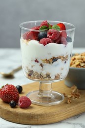 Tasty yogurt with fresh berries and granola in glass dessert bowl on white marble table, closeup