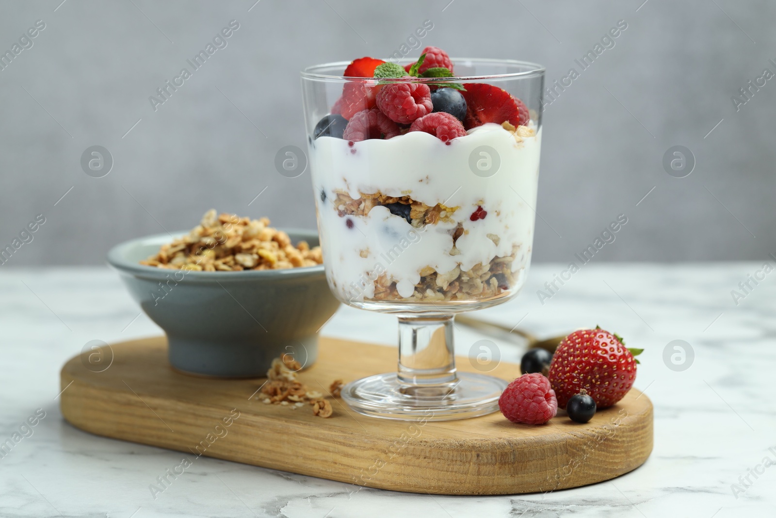 Photo of Tasty yogurt with fresh berries and granola in glass dessert bowl on white marble table, closeup