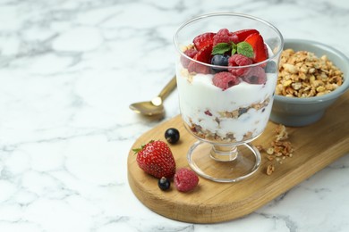 Tasty yogurt with fresh berries and granola in glass dessert bowl on white marble table, closeup. Space for text