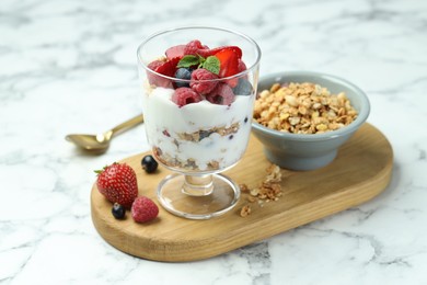 Photo of Tasty yogurt with fresh berries and granola in glass dessert bowl on white marble table