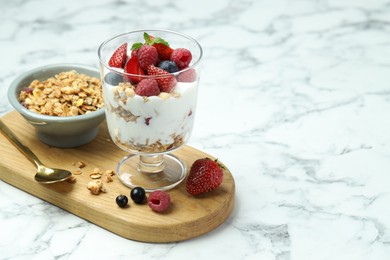 Tasty yogurt with fresh berries and granola in glass dessert bowl served on white marble table, space for text