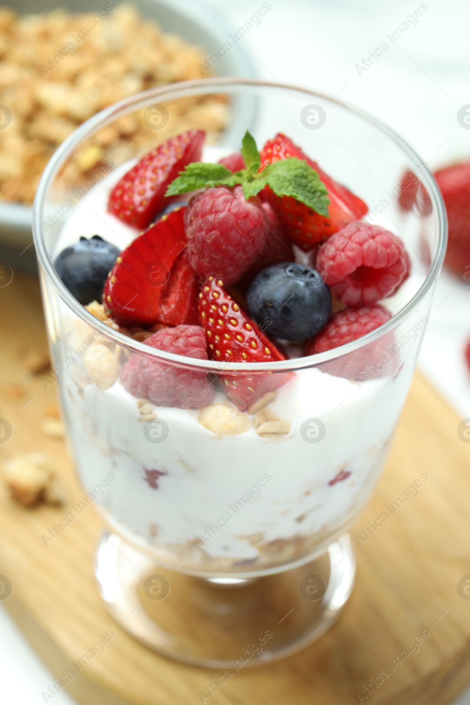 Photo of Tasty yogurt with fresh berries and granola in glass dessert bowl on table, closeup