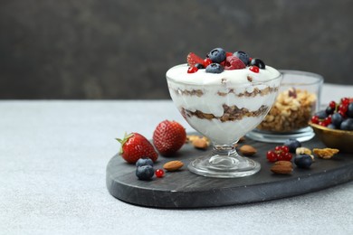 Photo of Tasty yogurt with fresh berries, granola and nuts on gray table, space for text