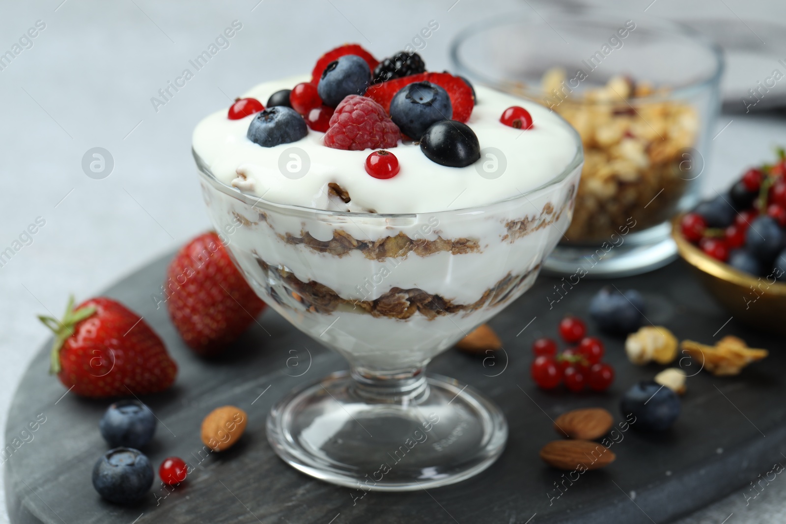 Photo of Tasty yogurt with fresh berries, granola and nuts on gray table, closeup