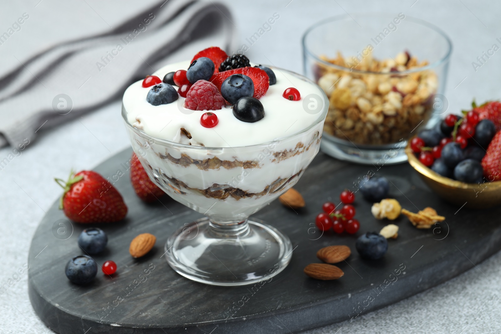 Photo of Tasty yogurt with fresh berries, granola and nuts on gray table, closeup