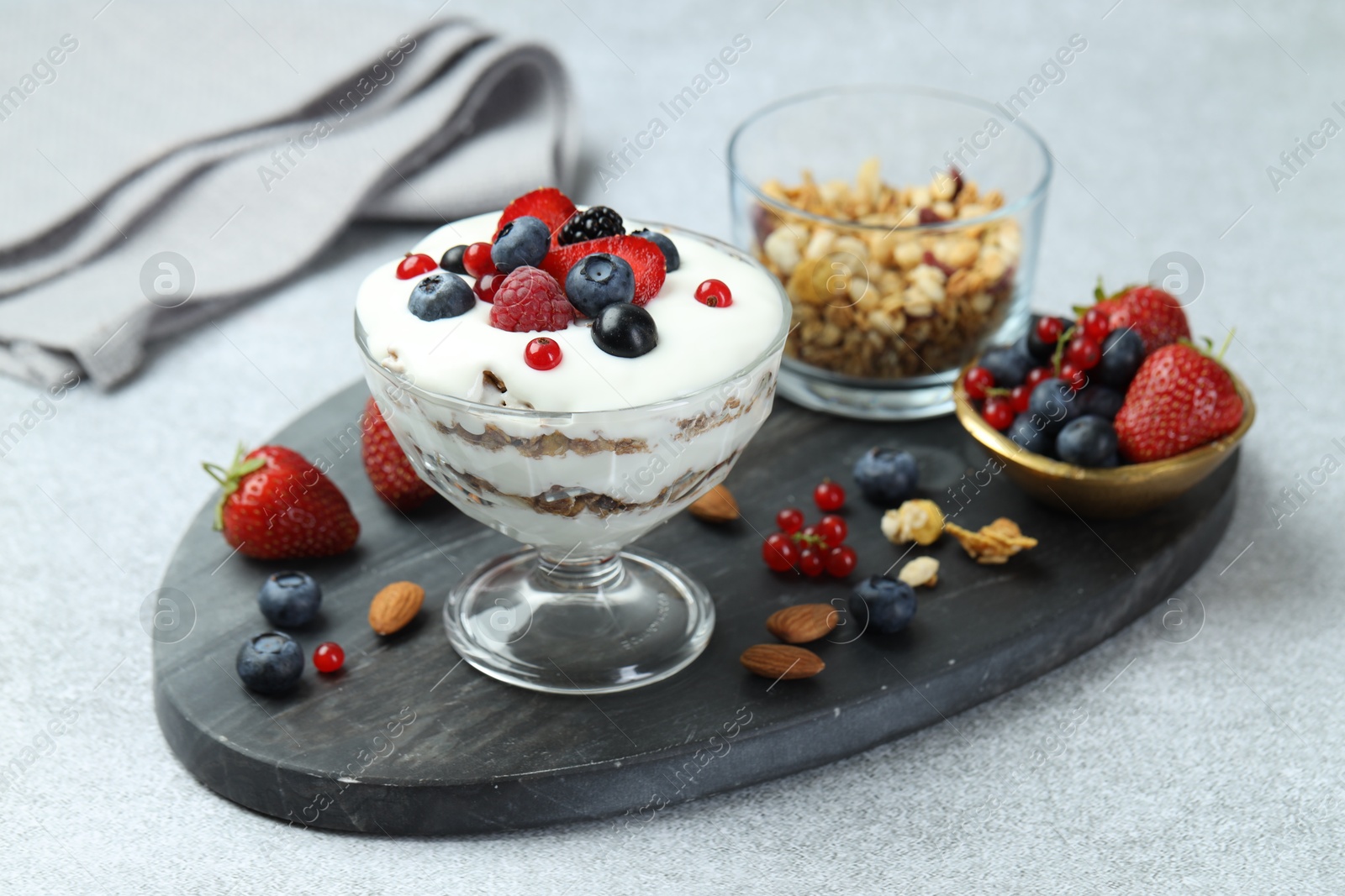 Photo of Tasty yogurt with fresh berries, granola and nuts on gray table, closeup