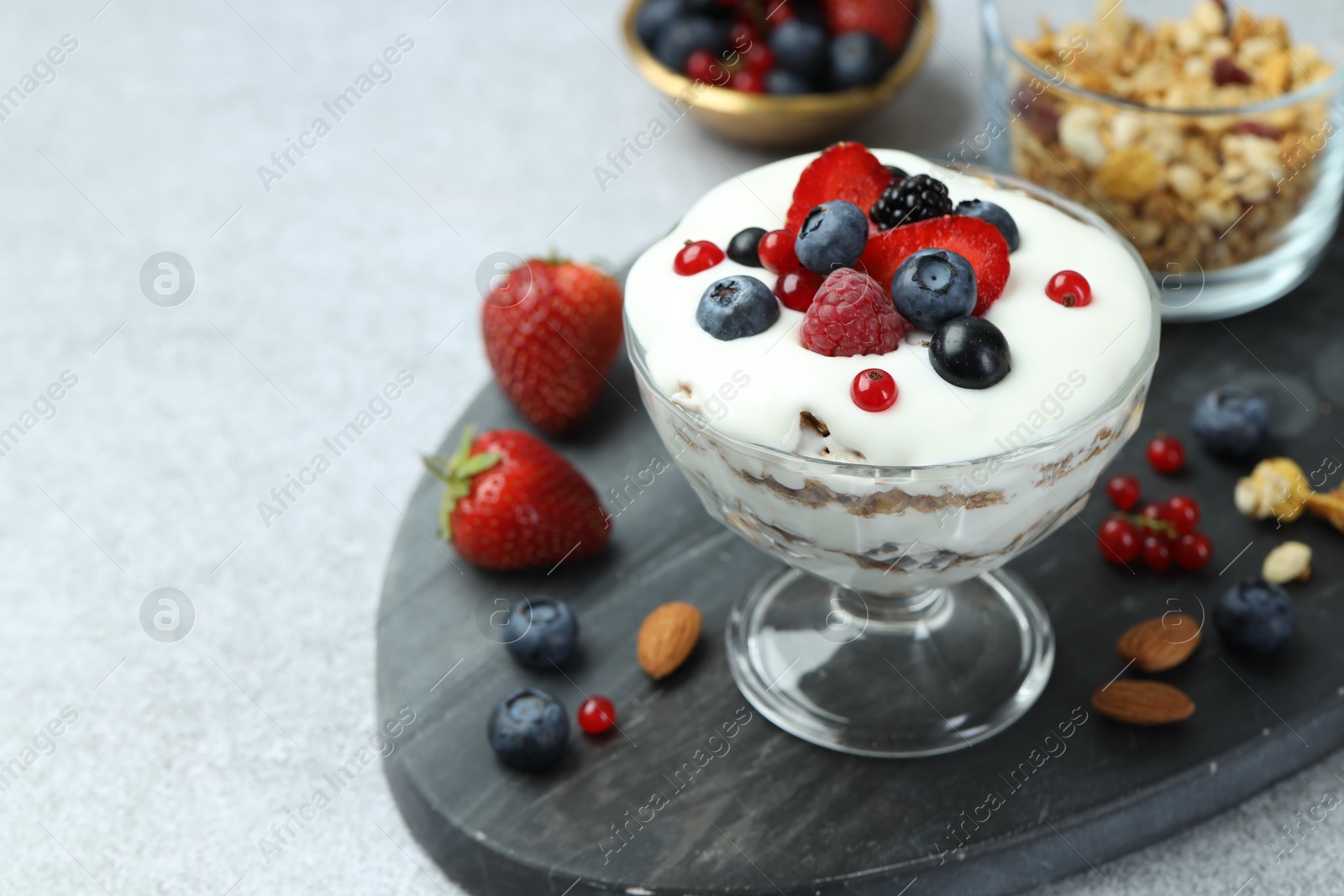 Photo of Tasty yogurt with fresh berries, granola and nuts on gray table, closeup. Space for text