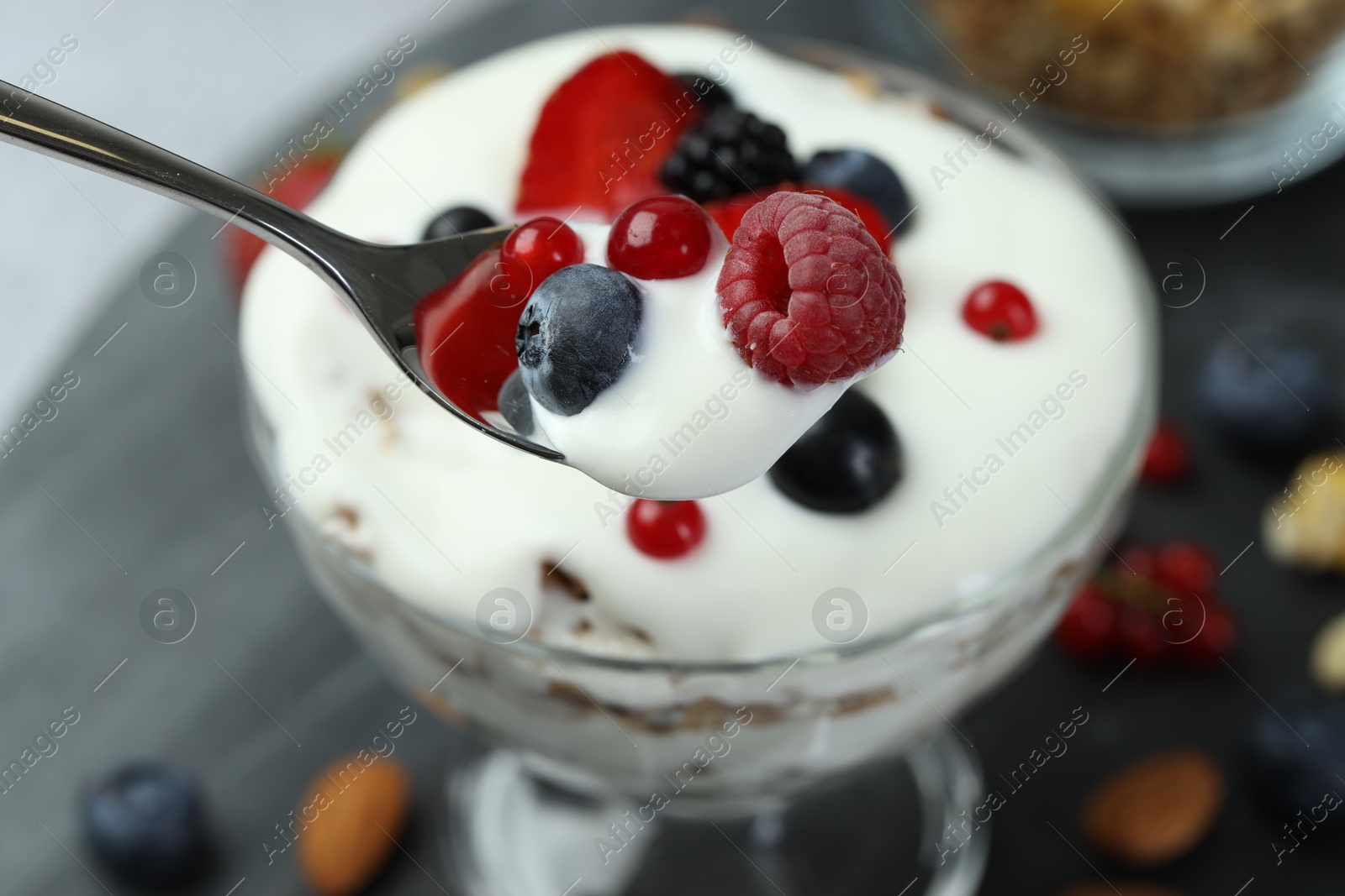 Photo of Taking tasty yogurt with fresh berries from glass dessert bowl at table, closeup