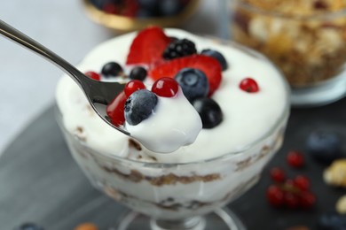 Taking tasty yogurt with fresh berries from glass dessert bowl at table, closeup