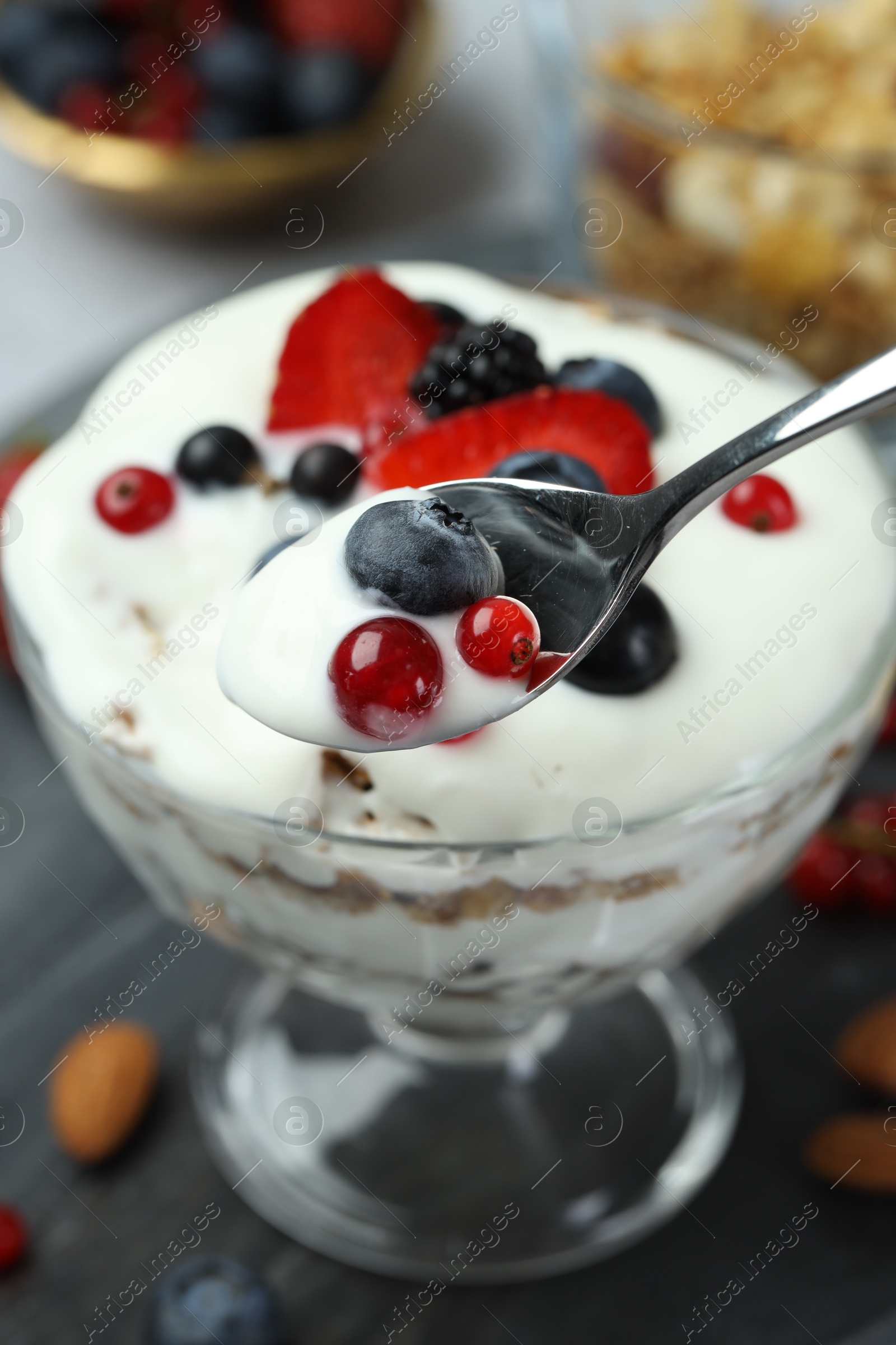 Photo of Taking tasty yogurt with fresh berries from glass dessert bowl at table, closeup