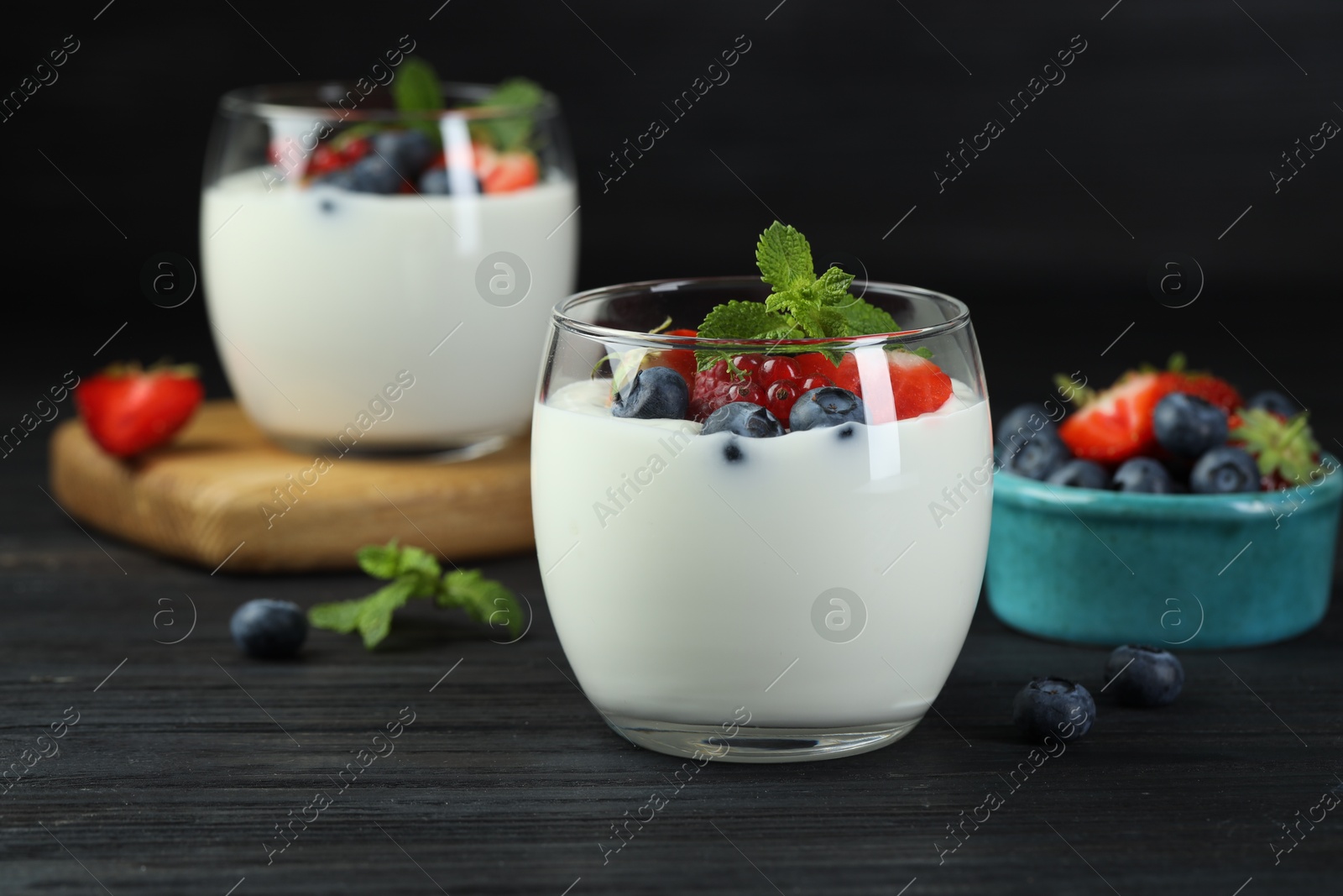 Photo of Tasty yogurt with fresh berries and mint in glasses on black wooden table, closeup