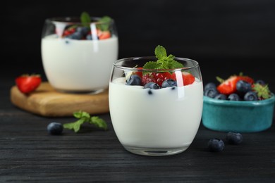 Photo of Tasty yogurt with fresh berries and mint in glasses on black wooden table, closeup