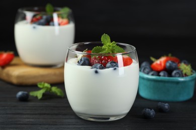 Photo of Tasty yogurt with fresh berries and mint in glasses on black wooden table, closeup