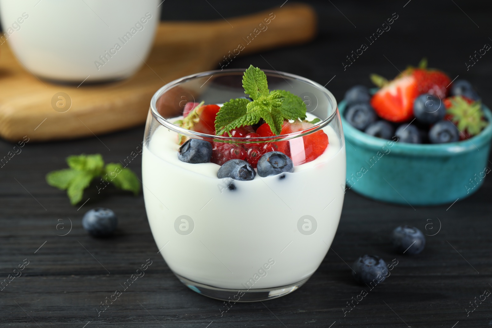 Photo of Tasty yogurt with fresh berries and mint in glass on black wooden table, closeup