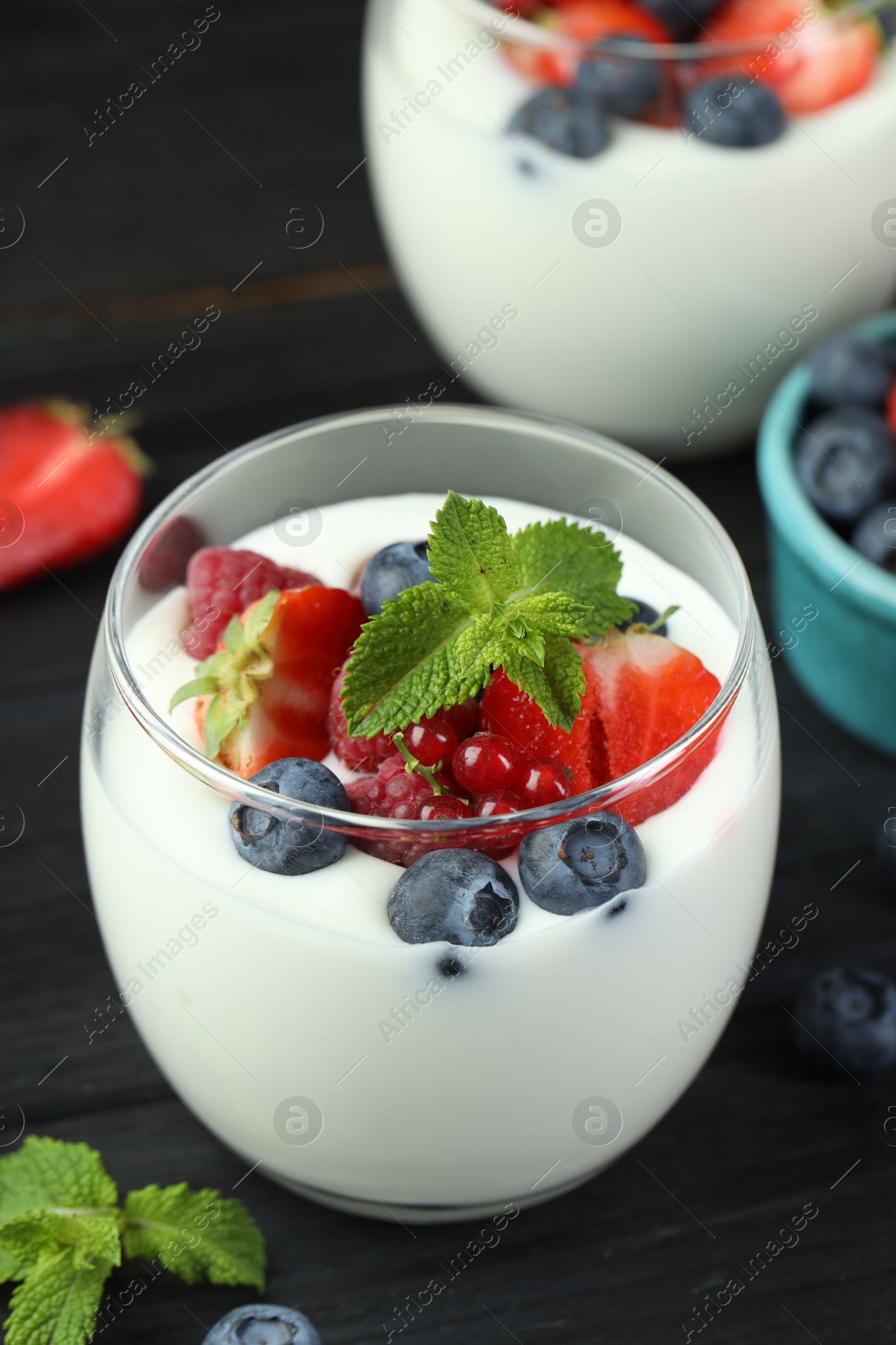 Photo of Tasty yogurt with fresh berries and mint in glasses on black wooden table, closeup