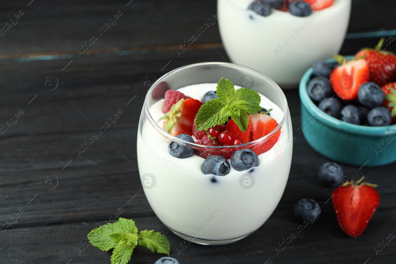 Photo of Tasty yogurt with fresh berries and mint in glasses on black wooden table, closeup. Space for text