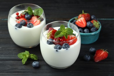 Photo of Tasty yogurt with fresh berries and mint in glasses on black wooden table, closeup