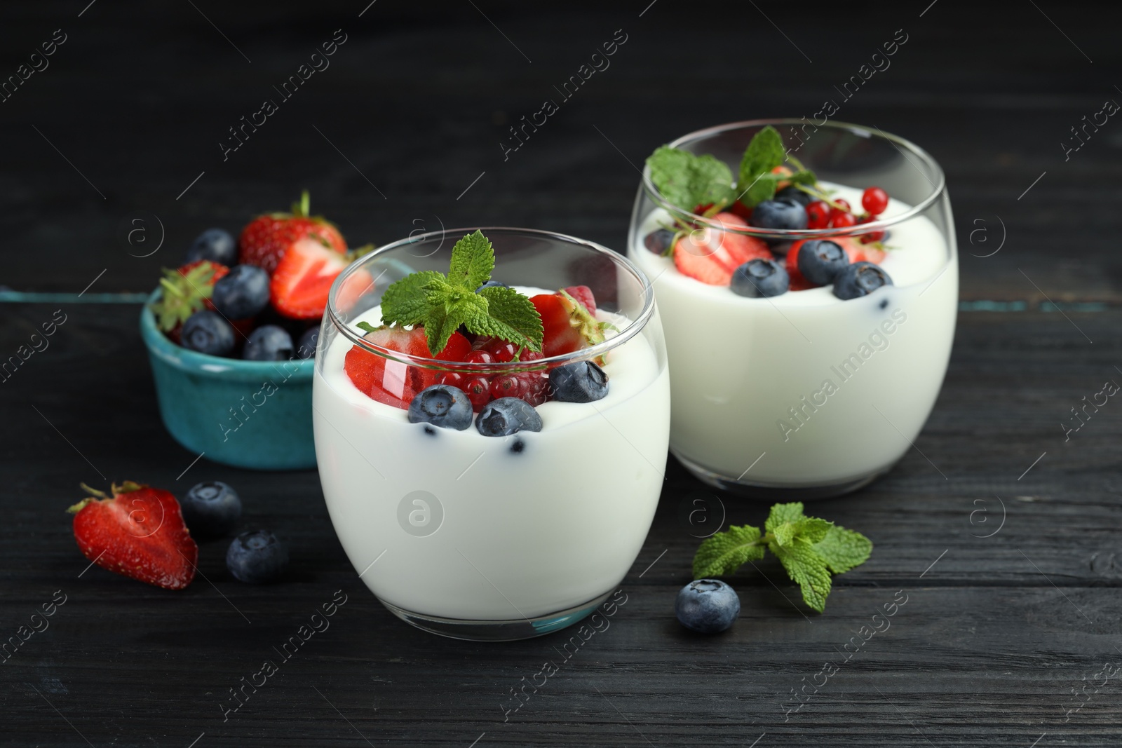 Photo of Tasty yogurt with fresh berries and mint in glasses on black wooden table, closeup