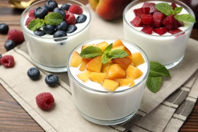 Tasty yogurt with fresh berries, fruits and mint in glasses on wooden table, closeup