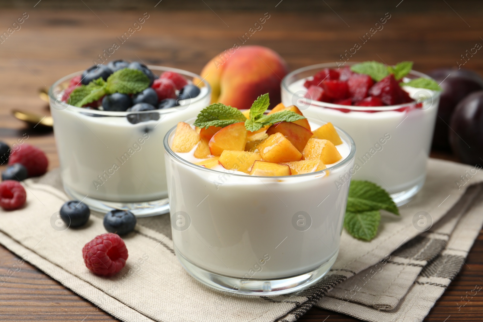 Photo of Tasty yogurt with fresh berries, fruits and mint in glasses on wooden table, closeup