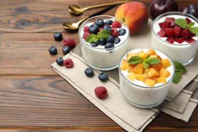 Photo of Tasty yogurt with fresh berries, fruits and mint in glasses on wooden table, closeup. Space for text