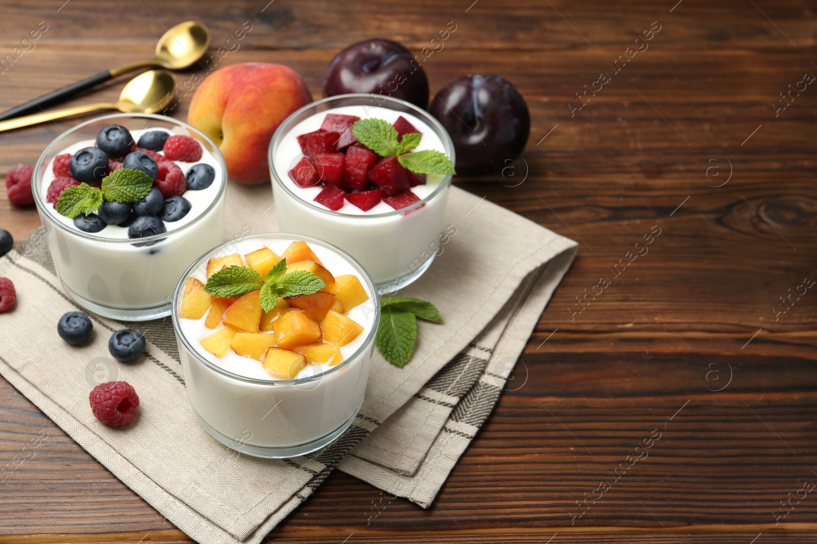 Photo of Tasty yogurt with fresh berries, fruits and mint in glasses on wooden table, closeup. Space for text