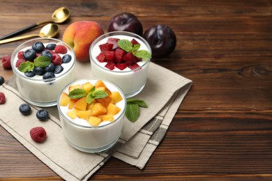 Photo of Tasty yogurt with fresh berries, fruits and mint in glasses on wooden table, closeup. Space for text