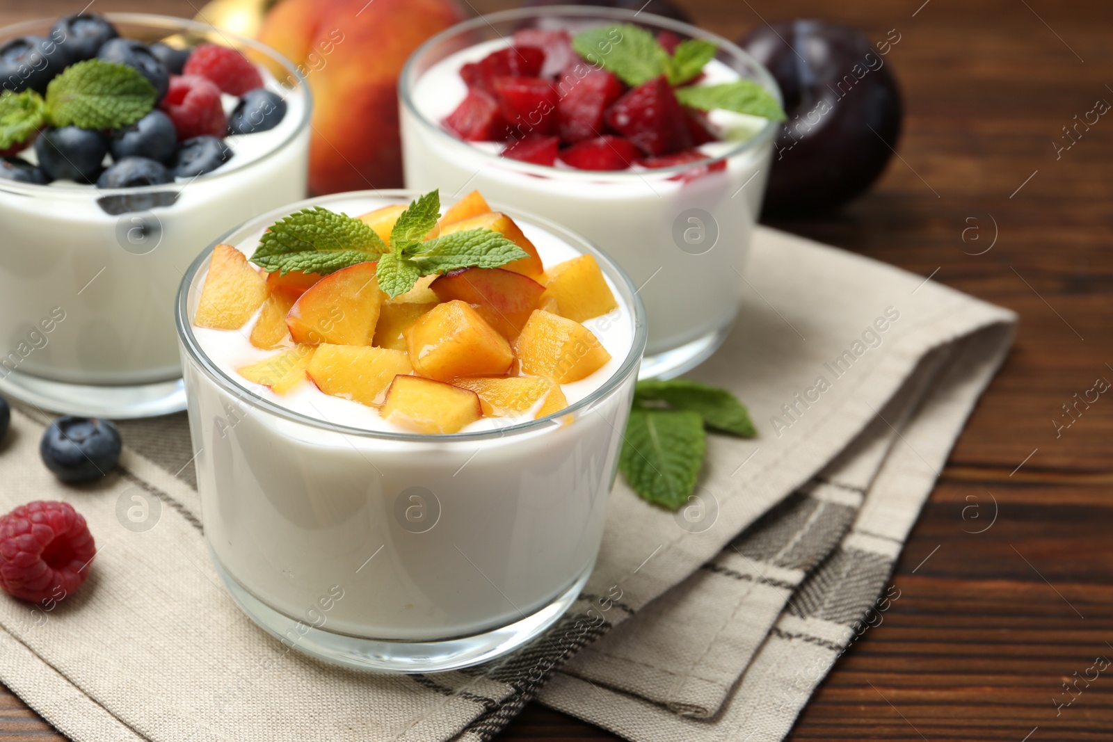 Photo of Tasty yogurt with fresh berries, fruits and mint in glasses on wooden table, closeup