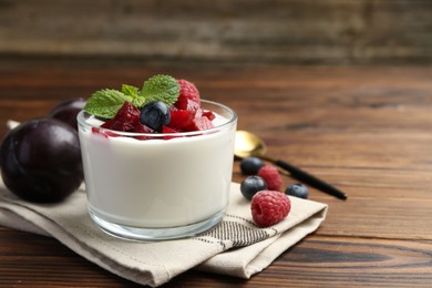 Photo of Tasty yogurt with fresh plums, berries and mint in glass on wooden table, space for text