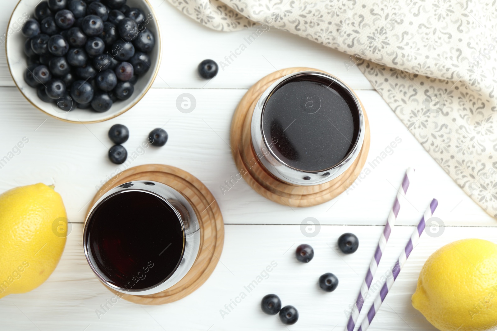 Photo of Tasty fresh acai juice in glasses with berries and lemons on white wooden table, flat lay