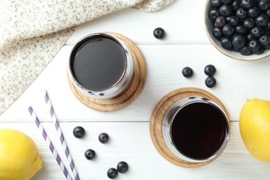 Photo of Tasty fresh acai juice in glasses with berries and lemons on white wooden table, flat lay