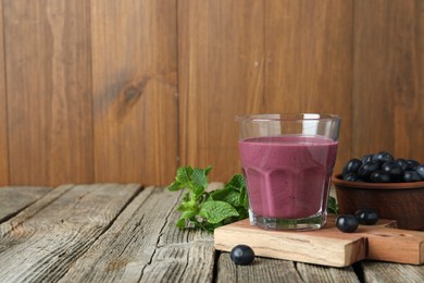 Photo of Tasty fresh acai juice in glass with berries and mint on wooden table, space for text