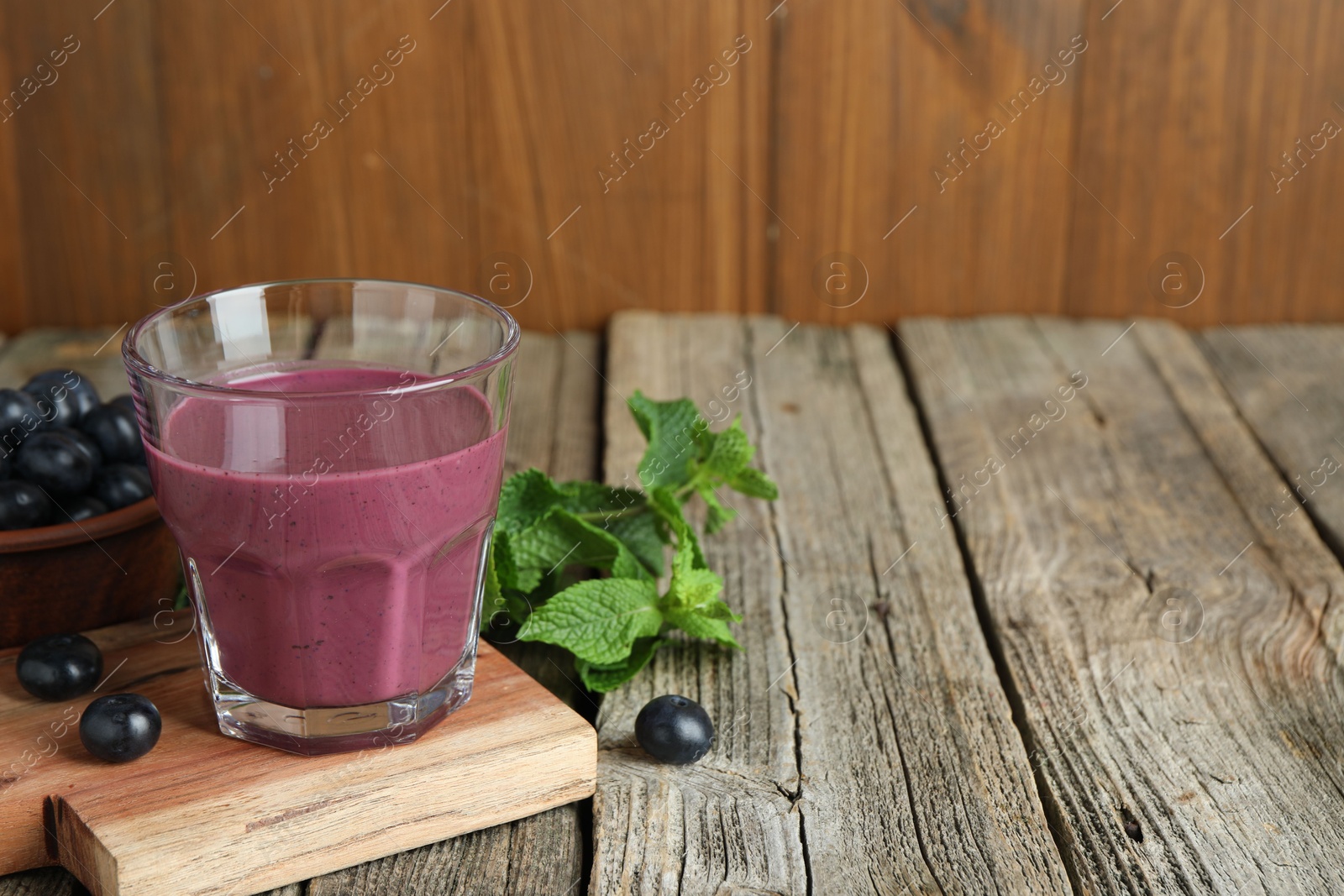 Photo of Tasty fresh acai juice in glass with berries and mint on wooden table, space for text