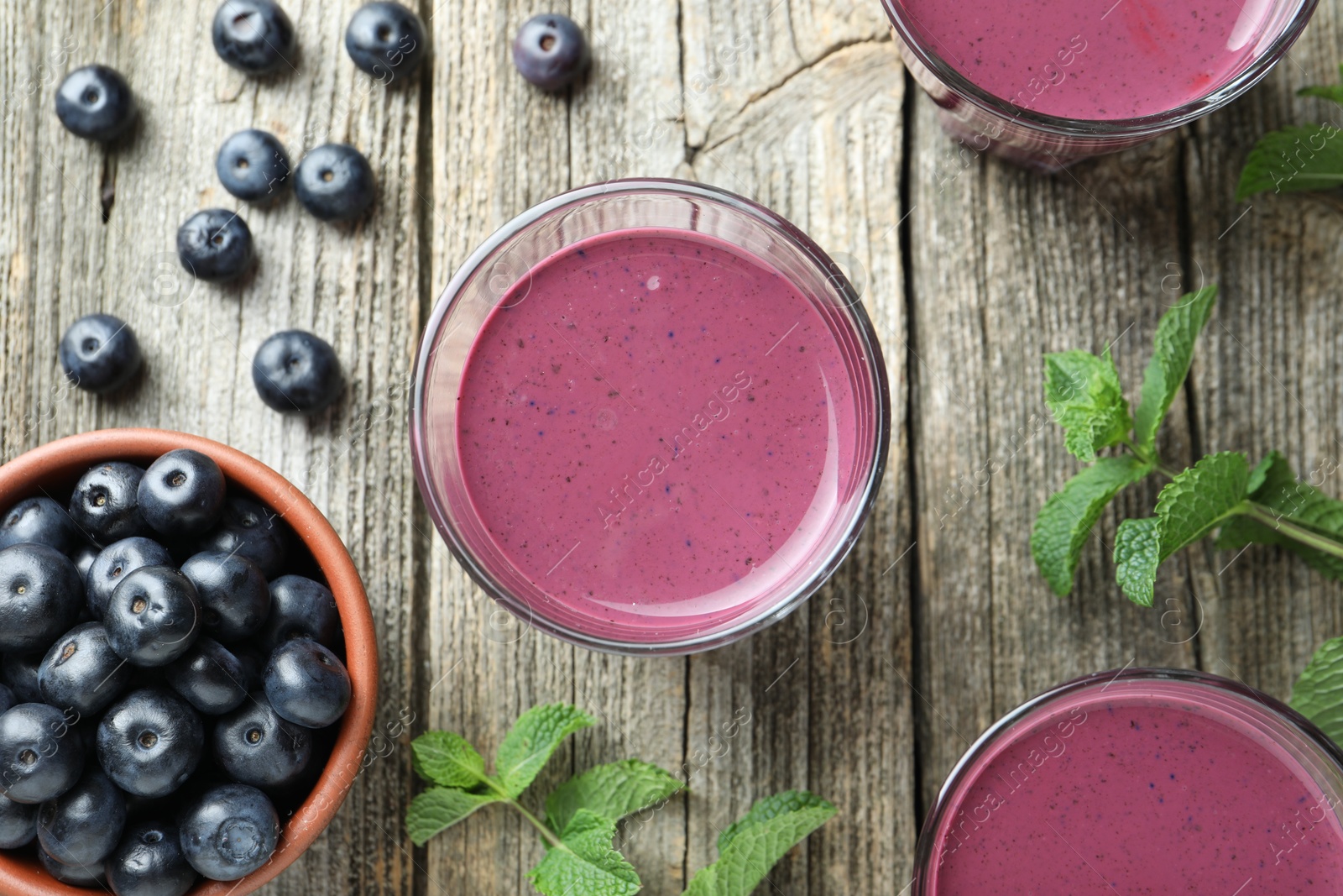 Photo of Tasty fresh acai juice in glasses with berries and mint on wooden table, flat lay