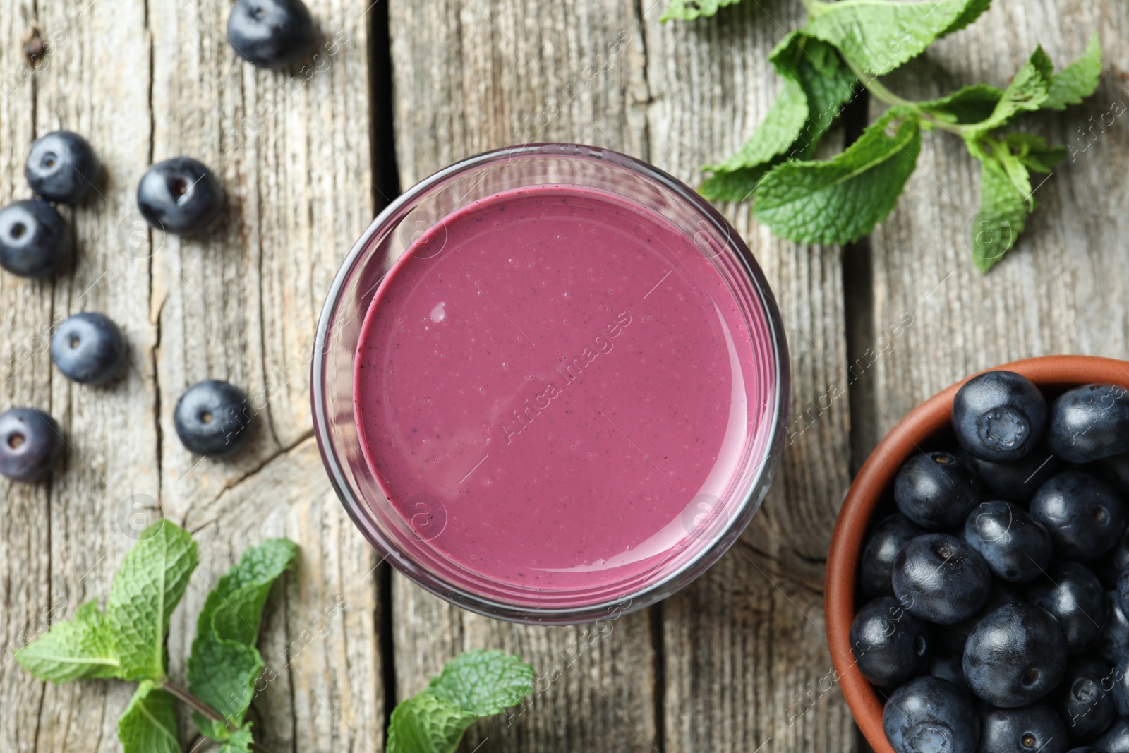 Photo of Tasty fresh acai juice in glass with berries and mint on wooden table, flat lay