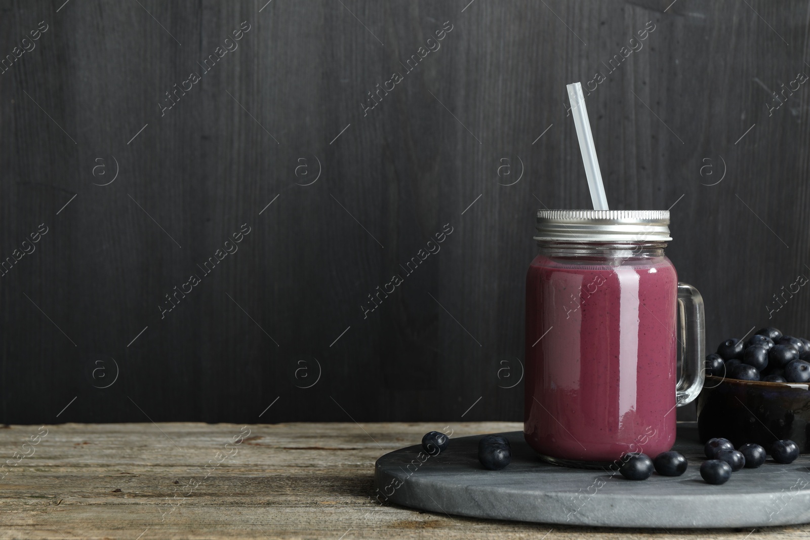 Photo of Tasty fresh acai juice in mason jar and berries on wooden table, space for text