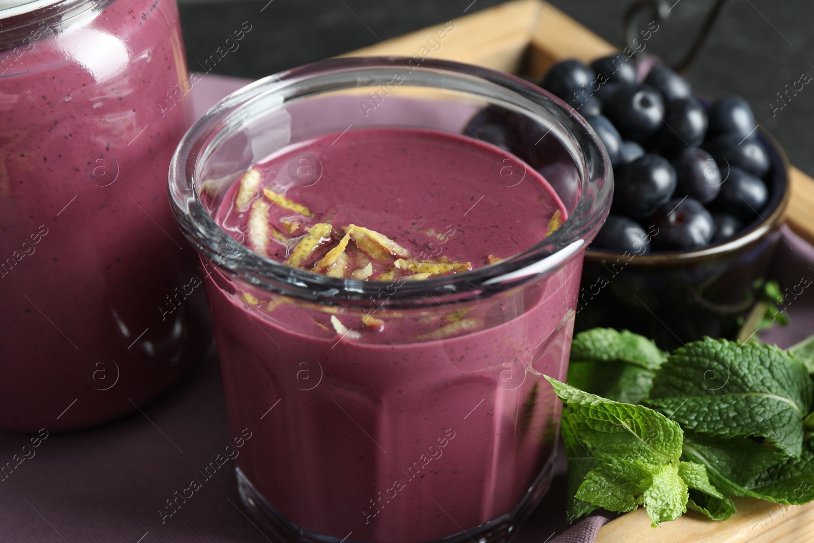 Photo of Tasty fresh acai juice with lemon zest, mint and berries on grey table, closeup