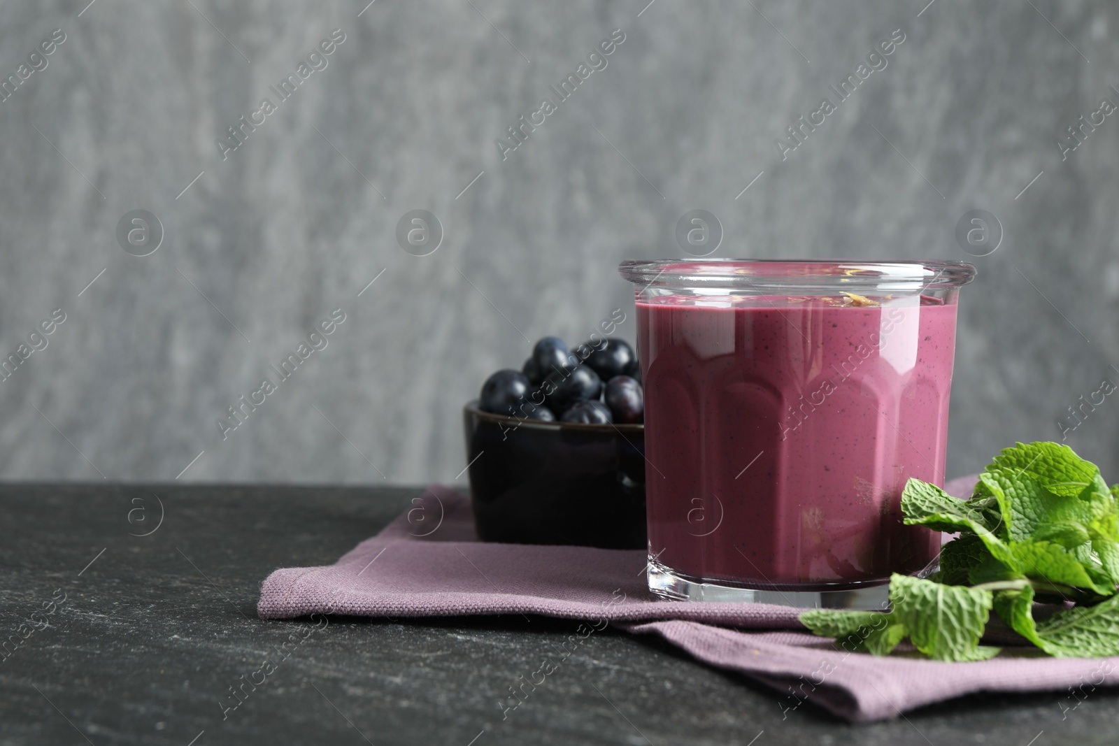 Photo of Tasty fresh acai juice in glass with mint and berries on grey textured table, space for text