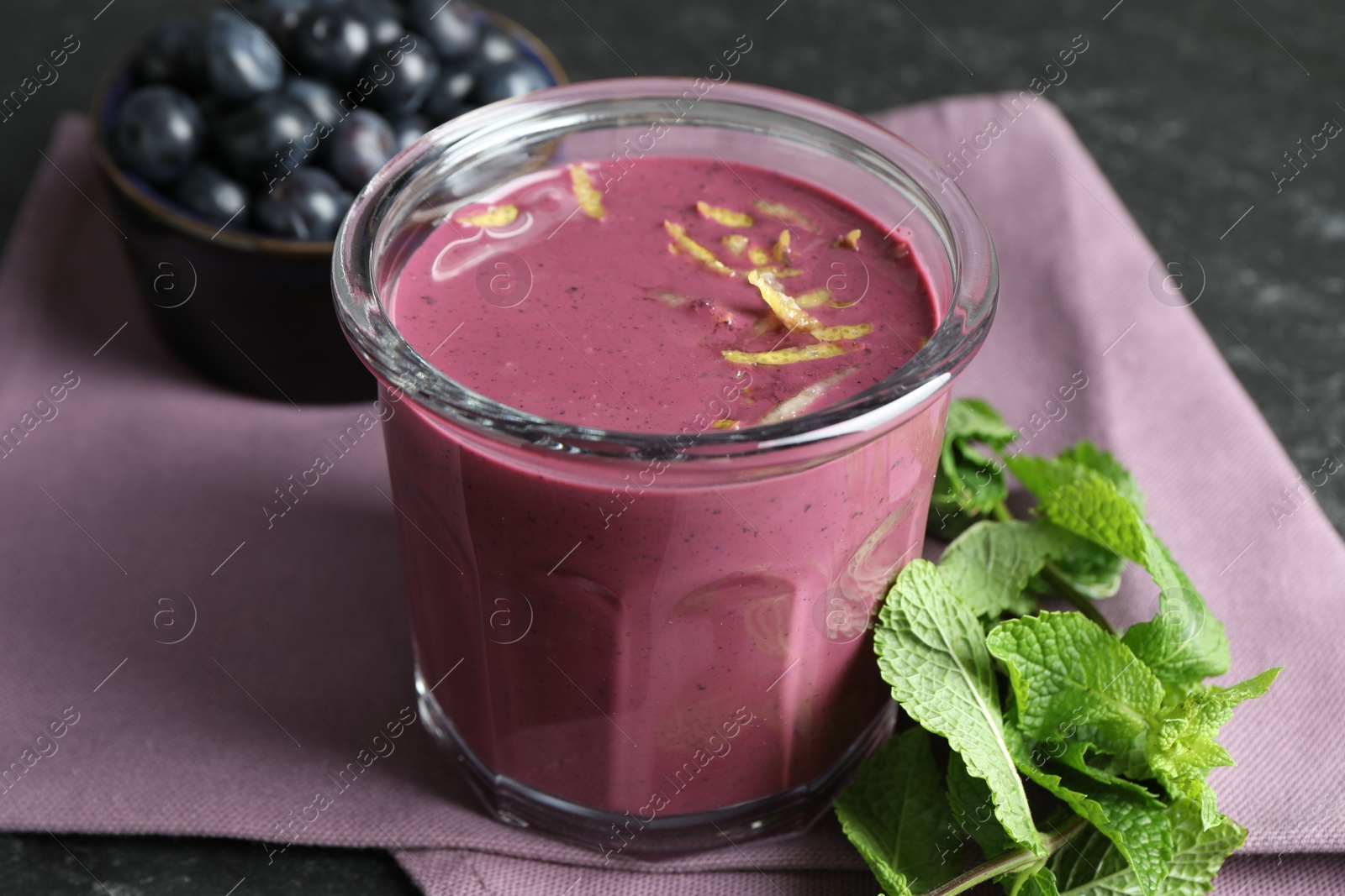 Photo of Tasty fresh acai juice with lemon zest in glass and mint on grey table, closeup