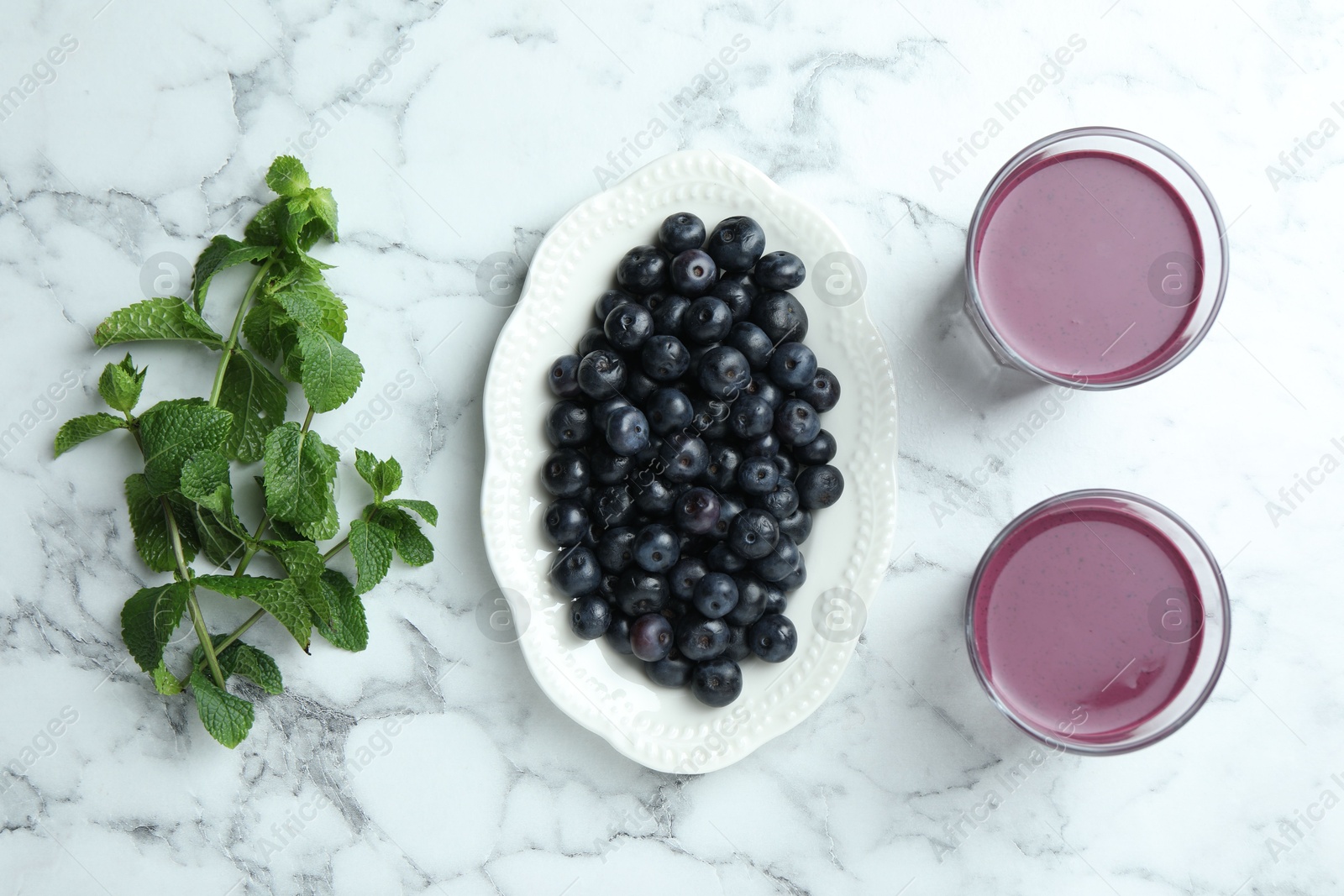 Photo of Tasty fresh acai juice in glasses, mint and berries on white marble table, flat lay