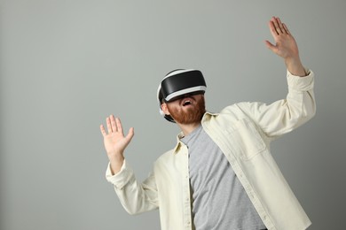 Photo of Emotional man using virtual reality headset on grey background. Space for text