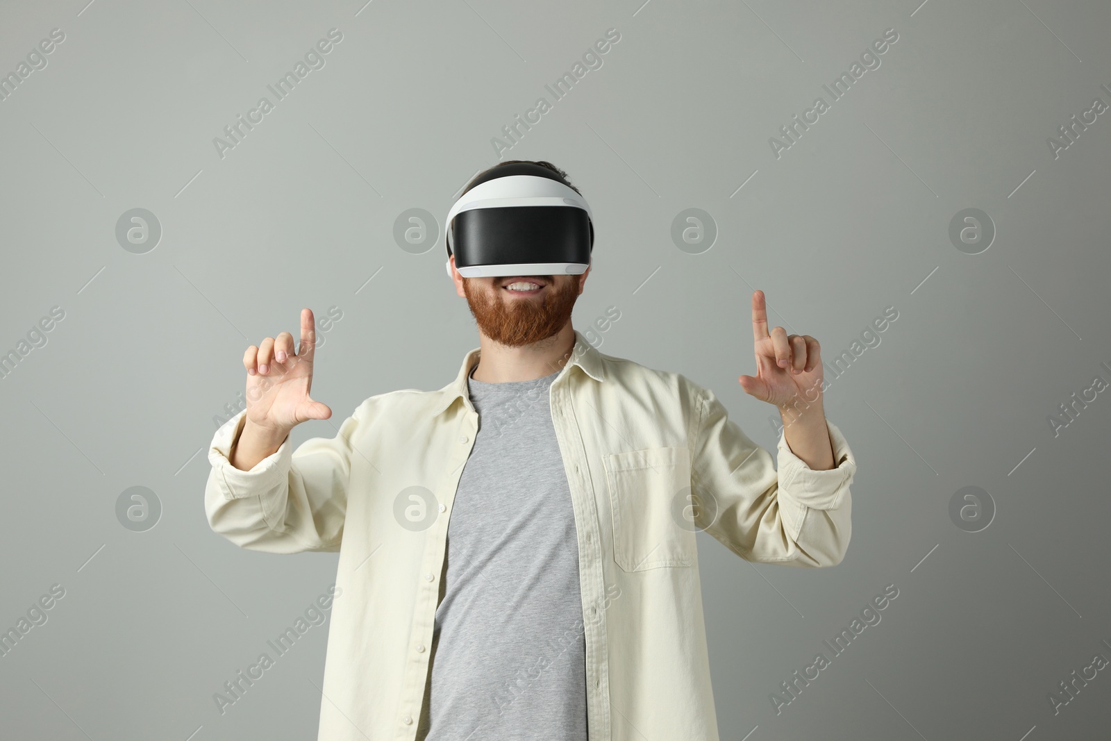 Photo of Smiling man using virtual reality headset on grey background