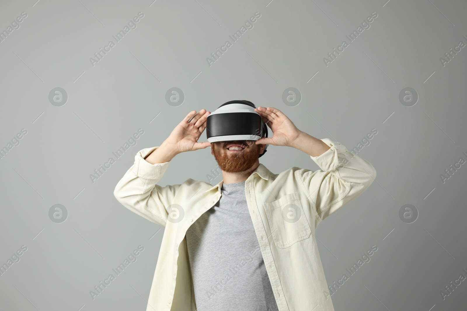 Photo of Smiling man using virtual reality headset on grey background