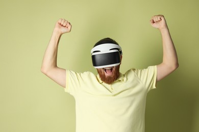 Photo of Emotional man using virtual reality headset on pale green background