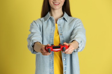 Photo of Happy woman playing video games with controller on yellow background, closeup